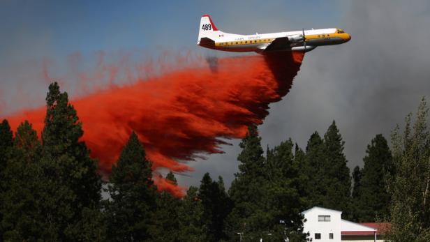 Ein Löschflugzeug sprüht rote Flüssigkeit über einen Wald.