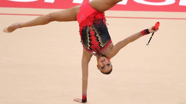 Eine rhythmische Sportlerin macht einen Handstand mit einem Gymnastikschläger in der Hand.