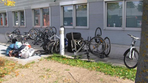 Vor einem Gebäude stehen mehrere Fahrräder und Fahrradteile.