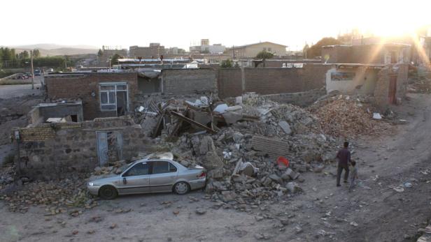 EPAepa03357985 A house in the western Iranian town of Varzeqan on 11 August 2012, which was devastated by an earthquake measuring 6 degrees on the Richter scale. Within 11 minutes of one another, two tremors registering magnitudes of 6.2 and 6 respective Ein beschädigtes Auto steht vor einem Haus, das durch ein Erdbeben zerstört wurde. Zwei Personen gehen vorbei.