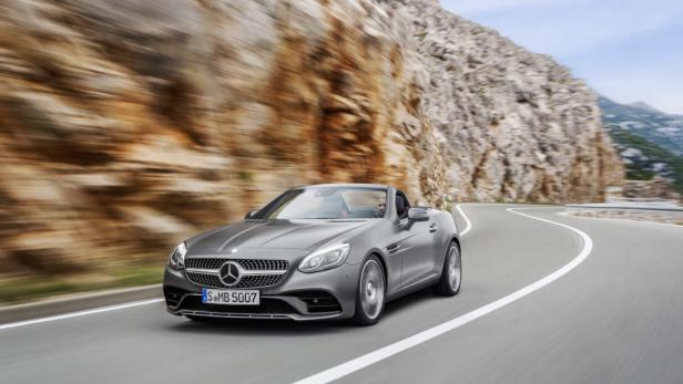 Ein grauer Mercedes-Benz SLK fährt auf einer kurvenreichen Straße entlang einer Felswand.