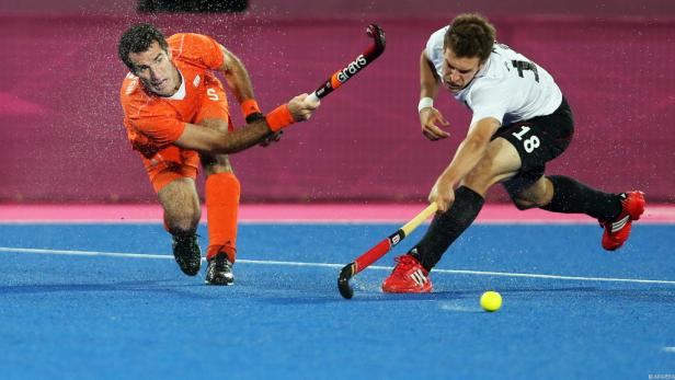 Zwei Hockeyspieler kämpfen um den Ball auf einem blauen Feld.