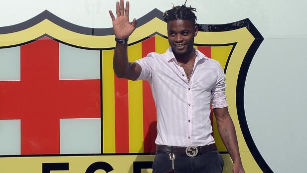 Ein lächelnder Mann mit Dreadlocks winkt vor dem Wappen des FC Barcelona.