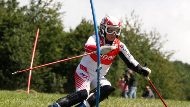 Eine Skifahrerin fährt auf einer Wiese Slalom.