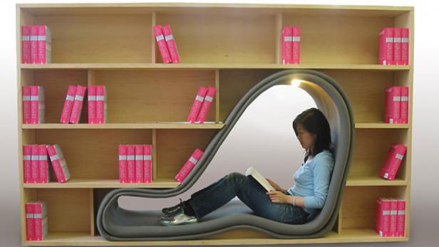 Eine Frau sitzt in einem Bücherregal mit integriertem Lesesessel und liest ein Buch.