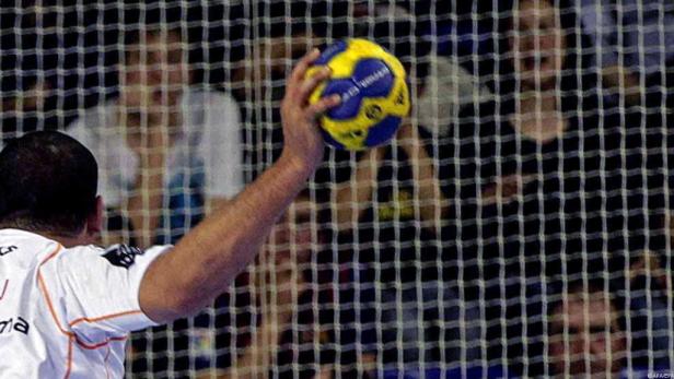 Ein Handballspieler wirft einen gelb-blauen Ball auf das Tor.