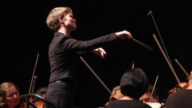 Eine Dirigentin leitet ein Orchester mit Streichinstrumenten.