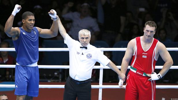 Ein Boxer in blau wird vom Ringrichter zum Sieger erklärt, während sein Gegner in rot daneben steht.