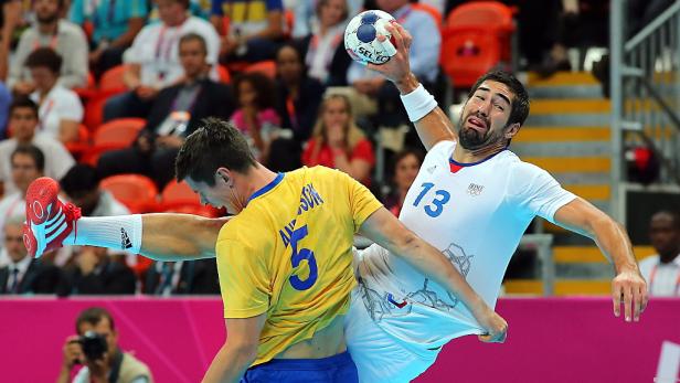 Ein Handballspieler versucht, einen anderen Spieler am Trikot zu ziehen, während er den Ball hält.