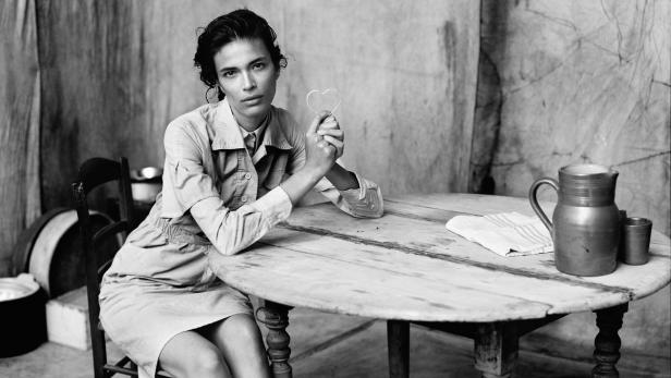 Eine Frau sitzt an einem Tisch und hält ein kleines Herz in der Hand.