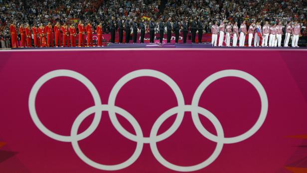Athleten verschiedener Nationen stehen bei einer Siegerehrung vor dem Hintergrund der Olympischen Ringe.