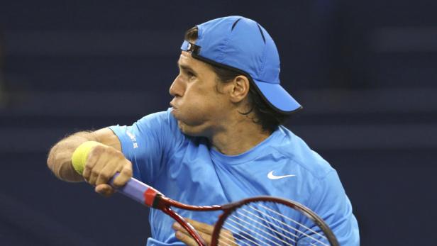 Ein Tennisspieler mit blauem Hemd und Kappe schlägt einen Ball.