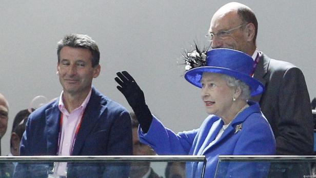 Königin Elizabeth II. winkt in einem blauen Kostüm und Hut.