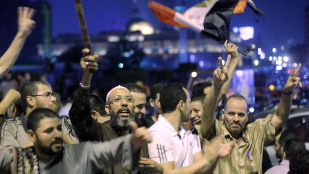 dapdThousands of supporters of Egypts Islamist President Mohammed Morsi celebrate in Tahrir Square, birthplace of the uprising that ousted Hosni Mubarak 18 months ago, in Cairo late Sunday, Aug. 12, 2012. Morsi ordered the retirement of the defense minist Eine Menschenmenge demonstriert mit erhobenen Händen und einer ägyptischen Flagge im nächtlichen Kairo.