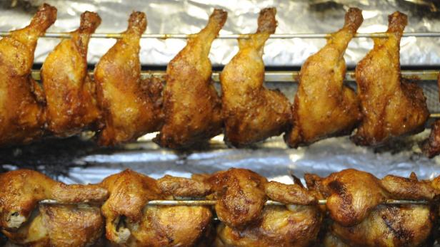Mehrere goldbraune Hähnchen und Hähnchenteile werden auf einem Grill zubereitet.