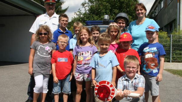 Eine Gruppe von Kindern posiert mit einem Polizisten vor einem Polizeiauto.