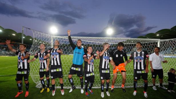 Eine Fußballmannschaft jubelt vor einem Tornetz auf einem grünen Rasen.