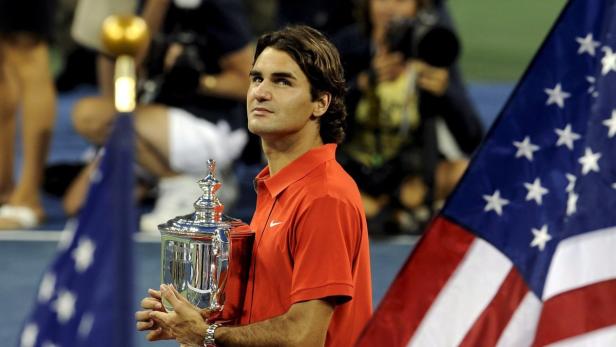 Roger Federer hält die Trophäe der US Open in den Händen, umrahmt von US-amerikanischen Flaggen.