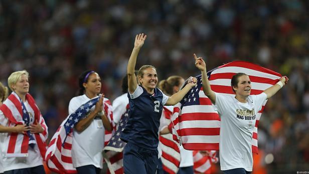 Das US-amerikanische Frauenfußballteam feiert mit der US-Flagge einen Sieg.