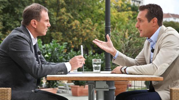 Zwei Männer sitzen an einem Tisch im Freien und diskutieren.