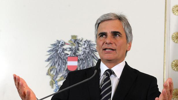 Ein Mann in Anzug gestikuliert vor dem österreichischen Wappen.