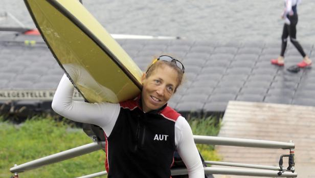 Eine Ruderin mit der Aufschrift „AUT“ trägt ein gelbes Ruderboot auf der Schulter.