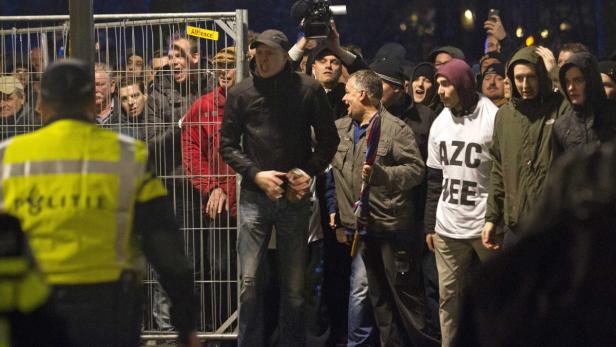 Eine Menschenmenge, darunter ein Polizist, steht hinter einem Gitter.