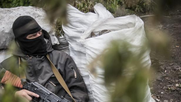 Ein Mann mit Sturmhaube und Gewehr lehnt an Sandsäcken.