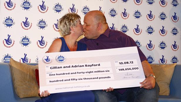 Gillian und Adrian Bayford küssen sich und halten einen Scheck über 148 Millionen Pfund.