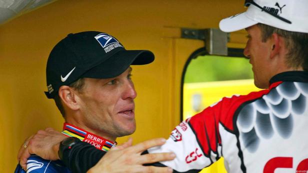 Lance Armstrong mit einer Kappe des United States Postal Service im Gespräch mit einer anderen Person.