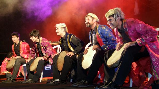 Eine Gruppe von Musikern in farbenfrohen Kostümen spielt auf Rahmentrommeln.