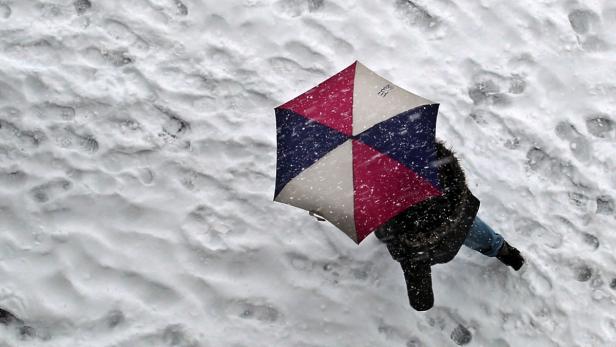 Eine Person mit einem Regenschirm geht durch den Schnee.