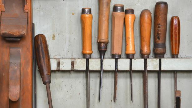 Mehrere Stecheisen mit Holzgriffen hängen an einer Wand.