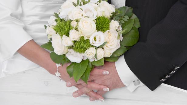 Ein Brautpaar hält einen weißen Rosenstrauß.