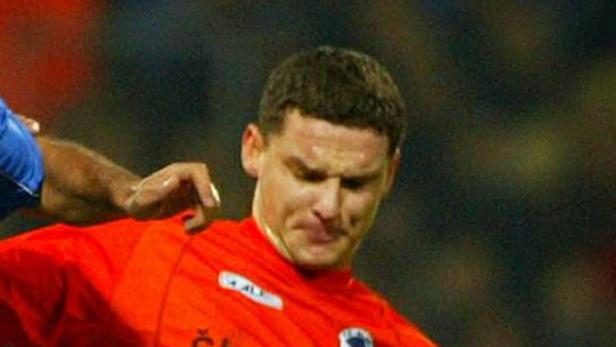 Ein Fußballspieler in einem orangefarbenen Trikot wird von einem anderen Spieler berührt.