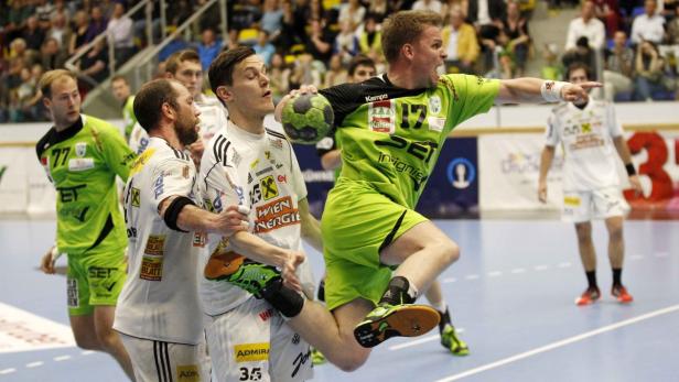 Ein Handballspieler in Grün springt, um den Ball zu werfen, während andere Spieler zusehen.