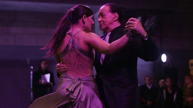 Ein Mann und eine Frau tanzen Tango in einem violett beleuchteten Raum.