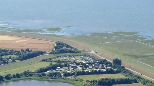 Ein Campingplatz liegt an der Küste, umgeben von Feldern und Wasser.