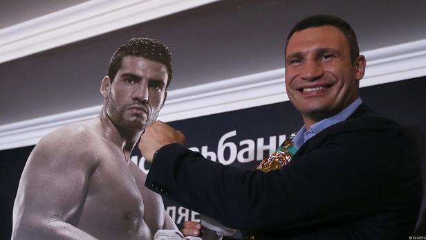 Wladimir Klitschko posiert vor einem Bild eines muskulösen Mannes.