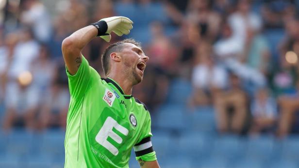 Ein Torwart in grüner Spielkleidung jubelt mit erhobenem Arm vor einer Zuschauertribüne.