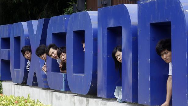 Mehrere Personen schauen aus den blauen Buchstaben des Wortes „FOXCONN“.