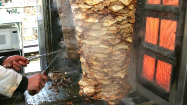 Ein Koch schneidet mit einem Messer Fleisch von einem Döner-Spieß.