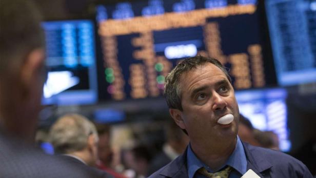 Ein Börsenhändler kaut Kaugummi vor einer Anzeigetafel mit Finanzdaten.