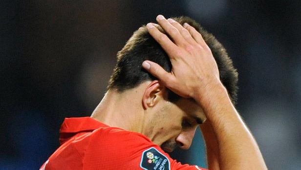 Ein Fußballspieler in rotem Trikot hält sich enttäuscht den Kopf.