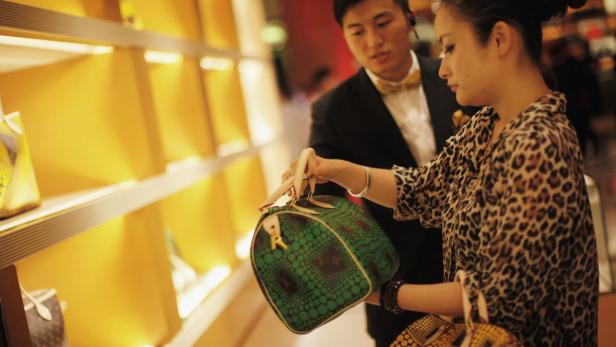 Eine Frau betrachtet in einem Geschäft eine grüne Louis Vuitton Tasche.
