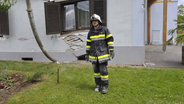 Ein Feuerwehrmann steht vor einem beschädigten Haus.