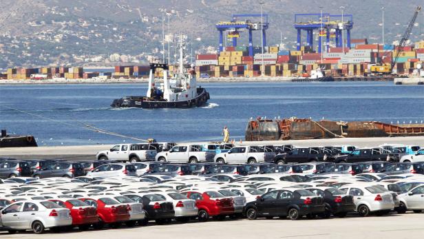 Ein Hafen mit einem Schlepper im Wasser und vielen geparkten Autos im Vordergrund.