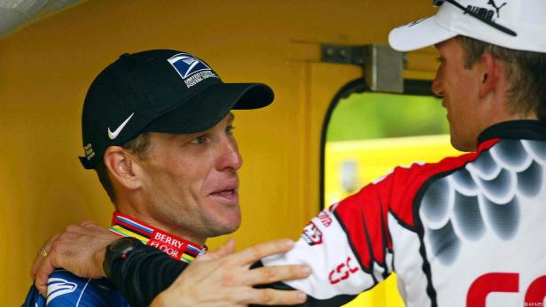 Lance Armstrong mit einer Kappe des United States Postal Service im Gespräch mit einem anderen Radfahrer.