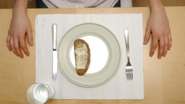 Ein Teller mit einem Stück Brot und Butter auf einem Tisch mit Besteck und einem Glas Wasser.