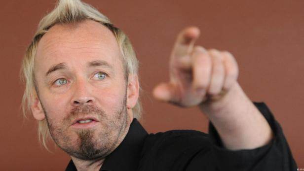 Ein Mann mit blonden Haaren und Bart zeigt mit dem Finger nach vorne.